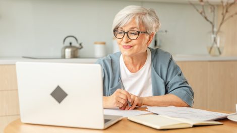 Idős nő ül a laptop előtt és mosolyog