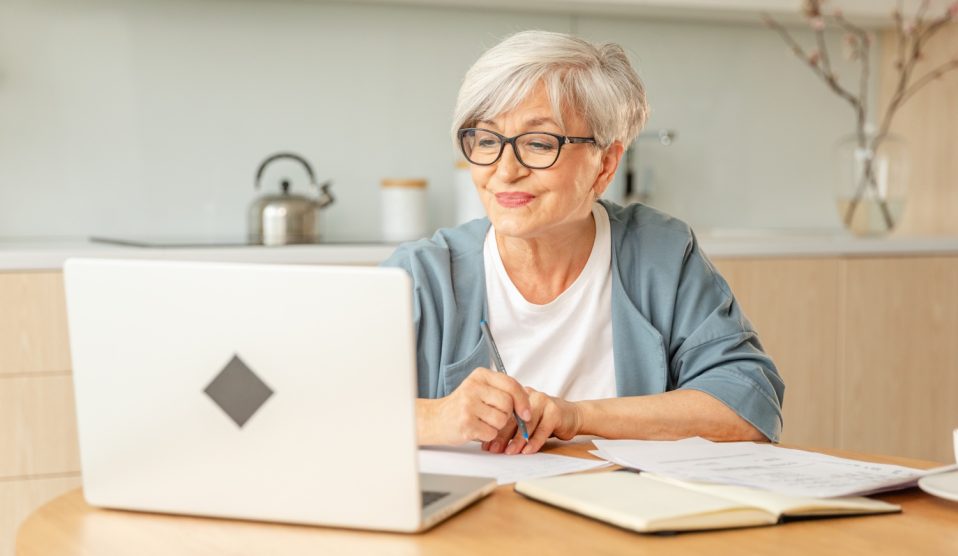 Idős nő ül a laptop előtt és mosolyog