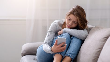 Egy lány szomorúan nézi a telefonját