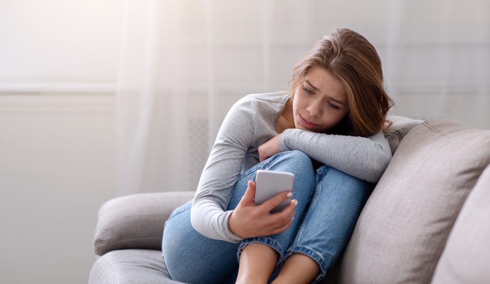Egy lány szomorúan nézi a telefonját