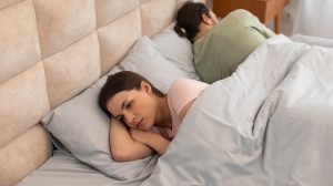 Felzaklatott nő fekszik az ágyban, háttal a férfinak